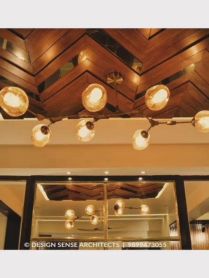 A stunning ceiling detail featuring a herringbone pattern in wood veneer, complemented by a modern, branching light fixture with globe bulbs.