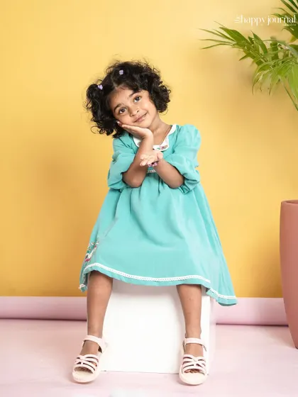 A girl with adorable curly hair poses in a lovely mint green dress. Her sweet, shy smile is absolutely heartwarming.