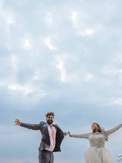 A feeling of pure freedom and joy. The couple holds hands with their arms outstretched against a vast, cloudy sky, as if they're about to fly.