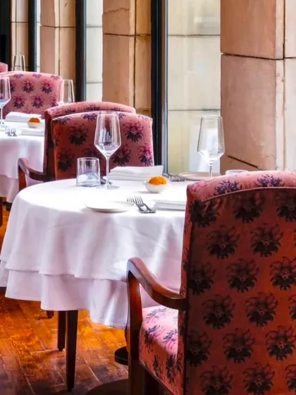 Tables are lined up in our sunlit dining room, ready for service. The warm wood floors and elegant chairs create a welcoming and sophisticated atmosphere.