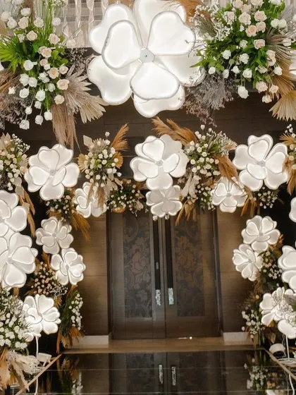 A closer look at the illuminated floral archway. The combination of large white blossoms, smaller white flowers, and rustic pampas grass creates a multi-layered and textured design.