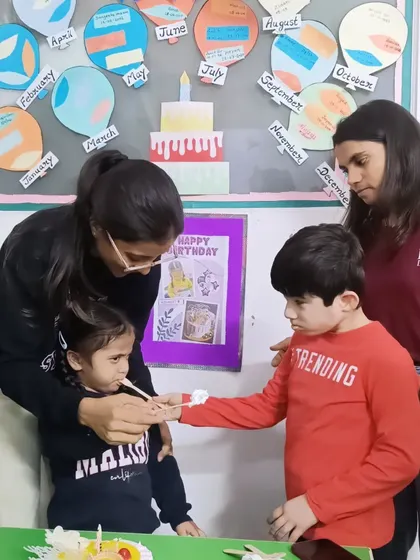 A teacher helps a child share a piece of birthday cake with a friend. This simple act teaches generosity and social interaction.