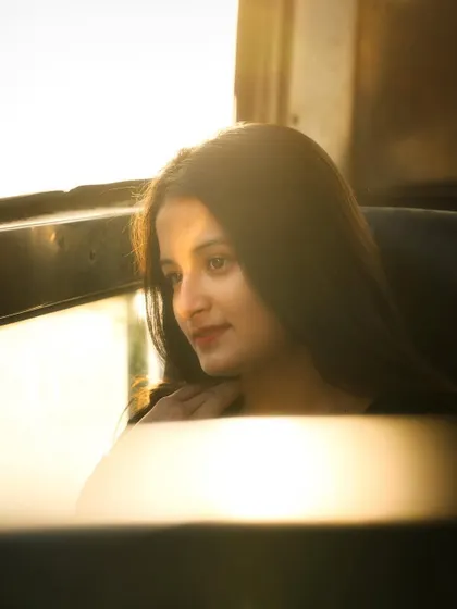 A beautiful golden hour portrait of a woman looking out a window. The warm, hazy sunlight creates a dreamy and flattering glow, perfect for capturing a soft and romantic mood.