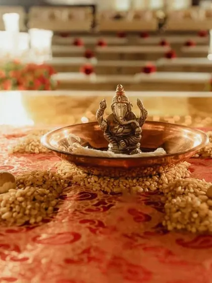 A close-up of the sacred ritual space, featuring a small Ganesha idol in a copper bowl, surrounded by grains and betel nuts on a rich red brocade cloth. Every detail is thoughtfully arranged to honor tradition.