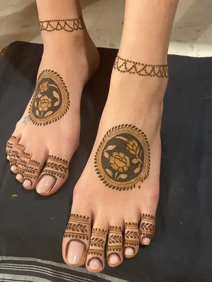 Minimalist feet mehendi with a central rose mandala and a delicate chain anklet. Proof that less can be more.