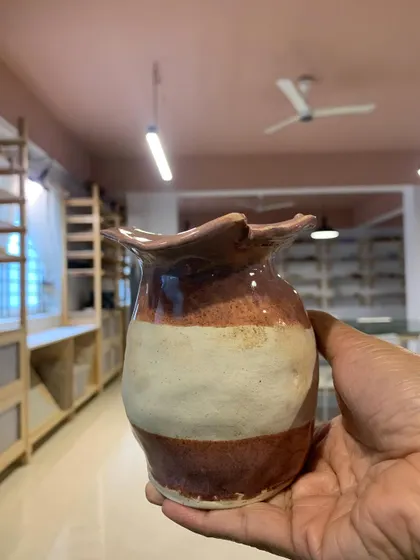 A beautiful two-toned vase with a ruffled rim, held up in our studio. This piece was created by a young student, showcasing their natural talent for form and color.