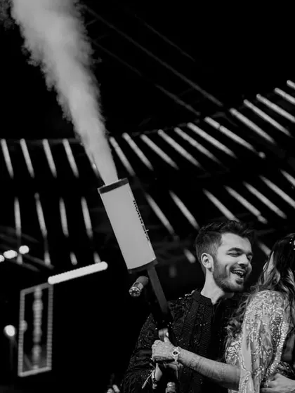The couple shares a moment on stage with a cold-pyro gun. This shot captures the fun, modern elements that make today's Sangeet performances so exciting.