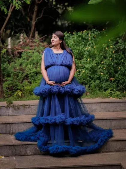 This full-length view shows the beautiful tiered ruffles and train of the royal blue maternity gown. It's a perfect rental choice for creating an elegant silhouette against a natural backdrop.
