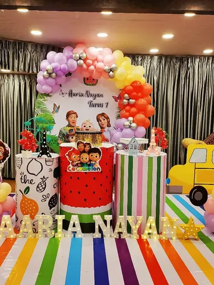 A Cocomelon party for Aaria Nayan's first birthday. This setup features a unique striped pedestal and a fruit-themed one, adding a fresh twist to the decor.