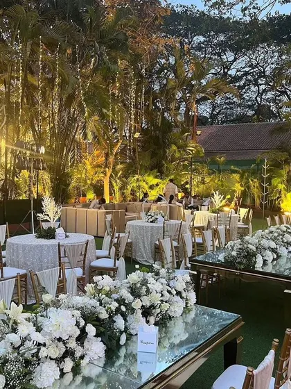 An evening view of the white and green themed engagement decor, with mirrored tables reflecting the beautiful floral centerpieces and warm lighting.