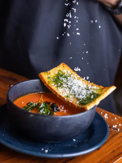 A chef sprinkles fresh parmesan over a bowl of Roasted Tomato Soup. This action shot captures the final touch that makes this simple soup so special.