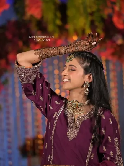 A happy bride dancing, her mehandi-covered arm raised in celebration.