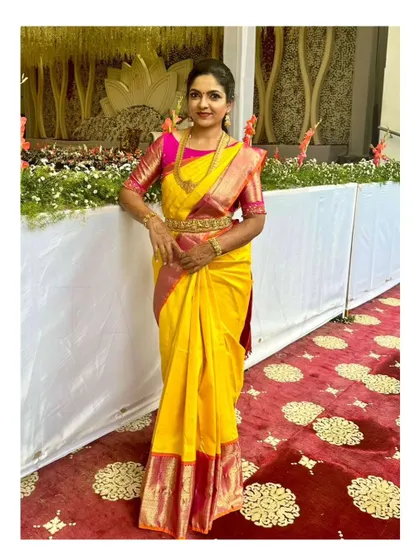 A full-length view of the client in her vibrant wedding attire, showing how the custom embroidered pink blouse perfectly complements her yellow Kanjivaram saree.