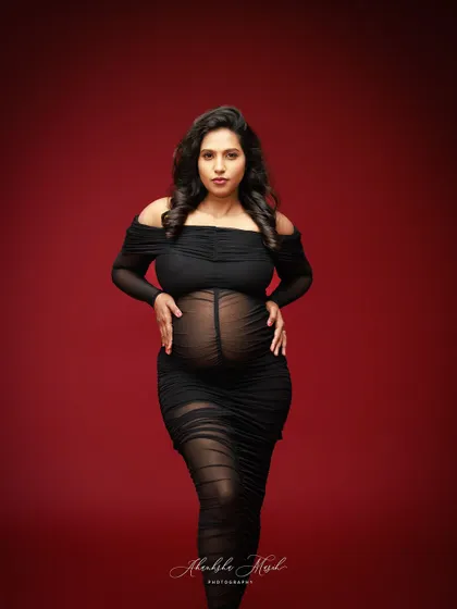 A powerful stance in a sheer black gown against a bold red backdrop, capturing the strength and beauty of the female form during pregnancy.