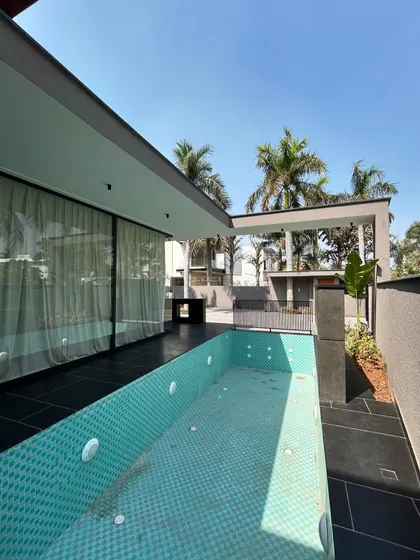 The jacuzzi and pool area at Gulmohar Farmhouse are designed for relaxation. The turquoise mosaic tiles of the pool contrast beautifully with the dark grey patio, while surrounding palm trees enhance the tropical, luxurious feel.