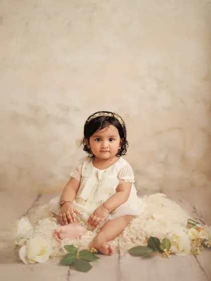 A full-length portrait of a baby girl celebrating her first milestone. The soft, neutral tones of the studio backdrop and her dress create a timeless and elegant image.