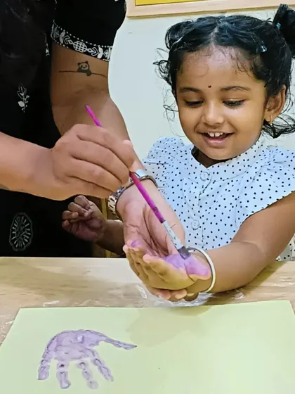 A teacher gently paints a little Aster's hand with purple paint. This one-on-one guidance helps even our youngest campers feel comfortable and confident during craft time.