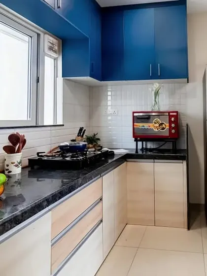 This kitchen combines royal blue upper cabinets with light wood base cabinets. The design is practical for daily use, with the refrigerator and sink area well-organized.
