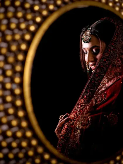 An artistic shot of the bride's reflection, framed by a golden mirror, highlighting the rich colors and textures of her wedding attire.
