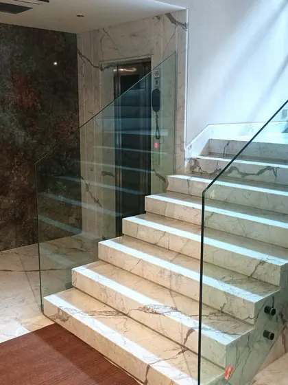 Another view of the side-mounted glass railing, showing its seamless integration with the luxurious marble steps and flooring.