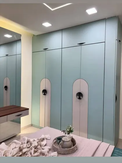 This is a look at a custom wardrobe we built for a client in Raj Nagar Extension. The design features a calming pastel blue finish, unique arched panels, and sleek black hardware for a contemporary feel.
