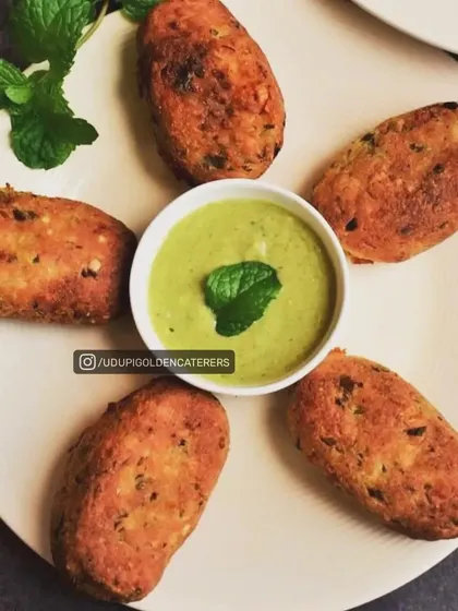 Golden-brown vegetable cutlets arranged neatly with a mint chutney dip. These patties are made with a mix of mashed vegetables and spices, offering a comforting and flavorful start to any meal.