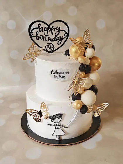 A whimsical two-tier cake with a hand-painted girl holding a cascade of chocolate balloons. Decorated with golden butterflies, this design is perfect for a sophisticated yet playful birthday celebration.