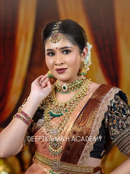 A classic portrait of a South Indian bride looking directly at the camera. Her look is defined by the rich temple jewelry and a deep, bold lip color that complements her saree.