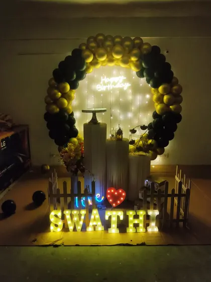 A simple yet chic black and gold balloon arch with a heart-shaped marquee light, perfect for an intimate birthday celebration.