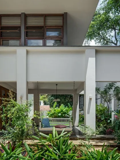 A view of the home's exterior, where clean white geometric forms interact with the lush garden. The design includes shaded outdoor living spaces that are integrated with the landscape.