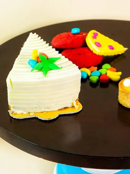 A detailed shot of a cake slice and other sweets on a dark wooden cake stand. The composition is playful and appetizing.