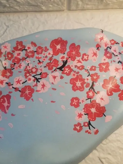 A close-up of another hand-painted cherry blossom cloud tray, this time on a soft blue background.
