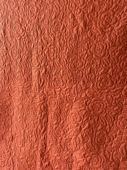 A close-up of the dense, floral longarm stitching on a reversible saree quilt, showing the texture and durability we add to each piece.