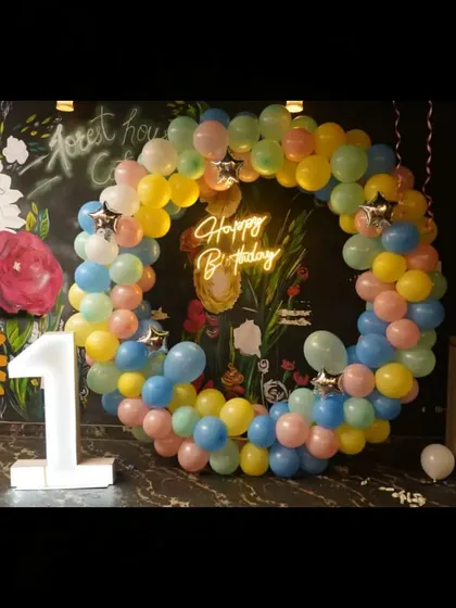 A first birthday party setup at a cafe, featuring a pastel balloon ring and a light-up number '1'.