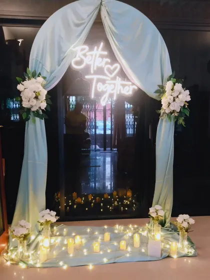 For this intimate home engagement, I created a romantic entryway using a soft pastel arch, white floral arrangements, and a custom 'Better Together' neon sign. The warm fairy lights and floor candles add a magical glow, perfect for evening celebrations.