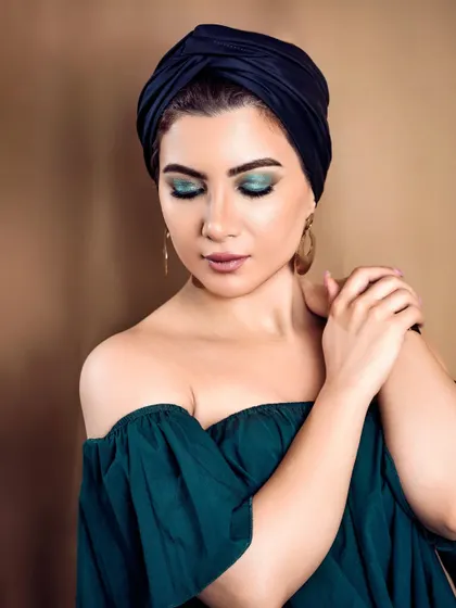 A beauty shot featuring vibrant turquoise eyeshadow, complemented by a black turban and gold earrings. The composition and color palette create a chic and classy portrait.