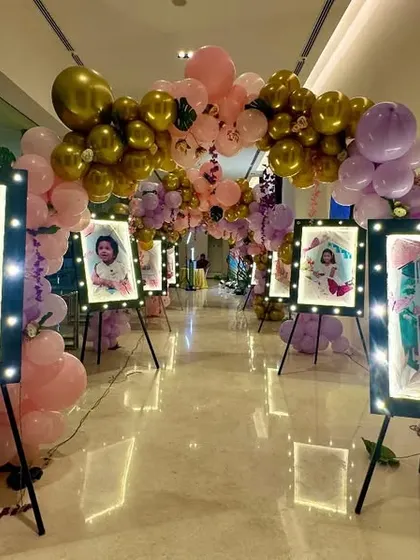 For this event entrance, I created a walkway lined with the couple's photos displayed on easels with built-in lights. The path is decorated with a balloon arch in gold, pink, and purple.