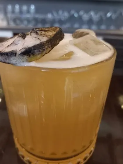 A close-up of a whiskey sour, showing the frothy top and dehydrated lime garnish.