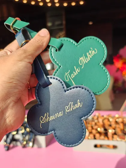 A close-up of the elegant calligraphy on green and blue leather luggage tags. The gold ink adds a festive and luxurious feel, perfect for a wedding celebration.