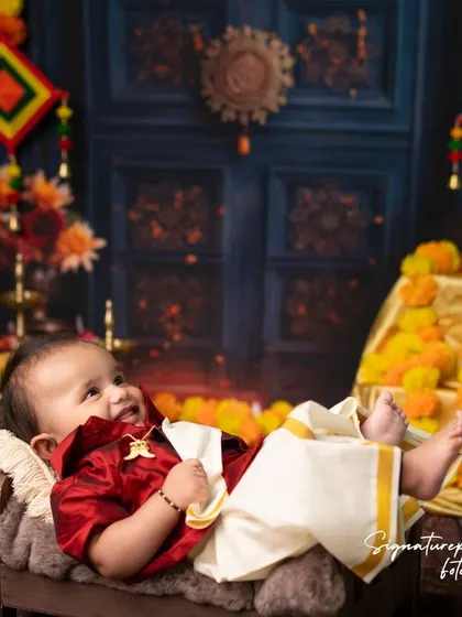 A happy baby enjoying his traditional photoshoot. Lying in a rustic wooden bowl, he is surrounded by mangoes and flowers, elements that are significant in many South Indian ceremonies.