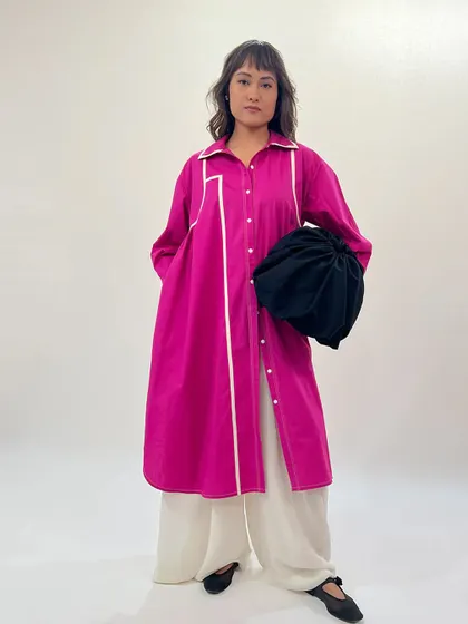 Draped in confidence, colored in power. This model wears a fuchsia shirt dress over wide-leg pants, accessorized with a black potli bag for a modern ethnic look.