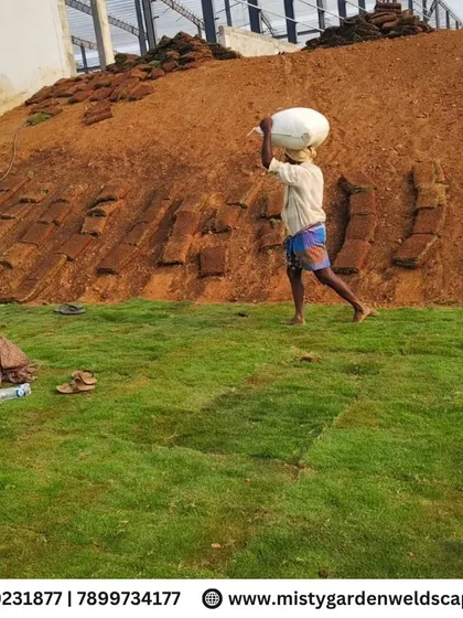 A worker carries a bag of supplies across the newly laid turf, showcasing the scale of this large farmhouse landscaping project.