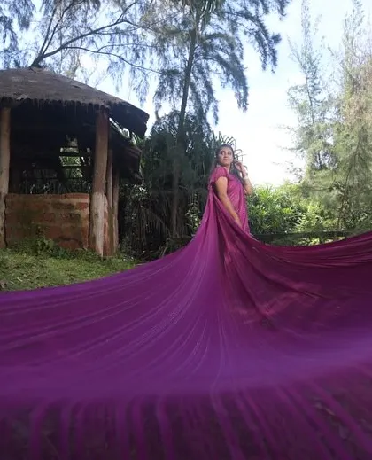 A vibrant purple long trail saree creating a massive, flowing look for a dramatic photoshoot in a rustic setting.