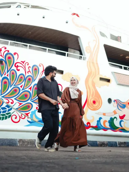 A full-length shot of the couple walking together, showcasing their outfits and the colorful, artistic backdrop of the ship.