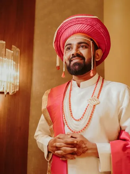 A portrait of a handsome Marathi groom in his traditional wedding attire, including the pink 'pheta' and pearl necklaces. He looks ready and excited for his wedding ceremony.