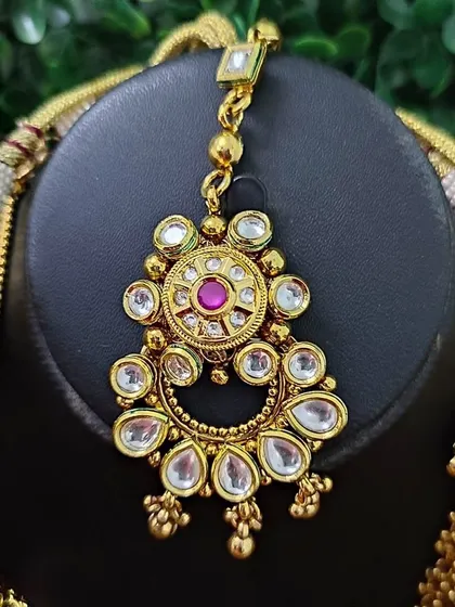 A close-up of the maang tikka from the temple-style bridal set. The intricate design features a central ruby-colored stone surrounded by kundan work.