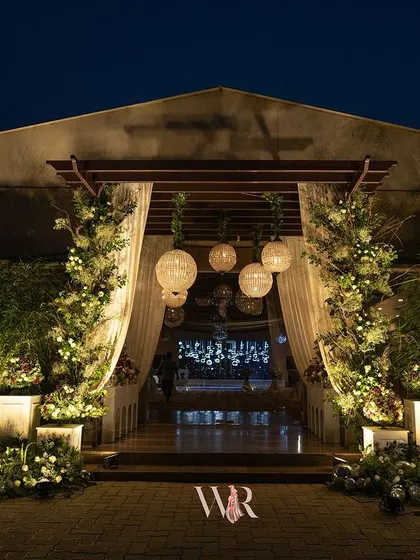 An enchanting entrance designed for an evening of elegance. We combined lush green foliage, soft white florals, and hanging paper lanterns to create a warm, inviting ambiance that perfectly complemented the venue's natural beauty.
