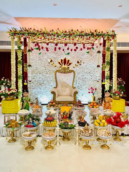 A beautiful all-white floral backdrop with red accents creates a very elegant and classic look. This setup for a baby shower combines a traditional frame with a modern color palette, complete with detailed plate arrangements and dolls.