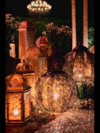 A collection of beautifully detailed Moroccan lanterns. The light filtering through the intricate patterns creates a warm, mesmerizing effect, essential for the Arabian Nights atmosphere.