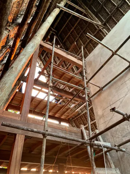 Looking up into the timber and thatch roof of the spa. The scaffolding shows the scale of the structure, which is designed to be both grand and intimate, with natural light filtering through the wooden beams.